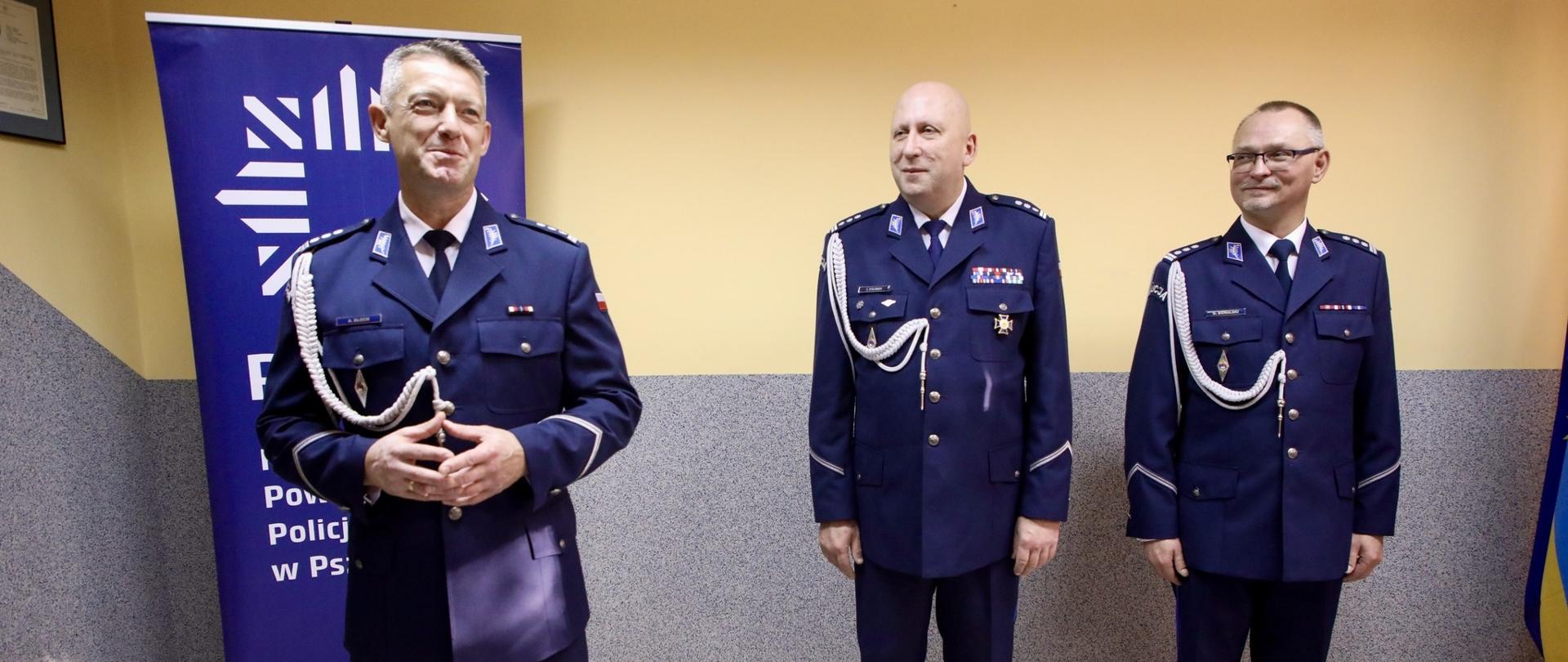 Trzech policjantów stoi przy żółtej ścianie