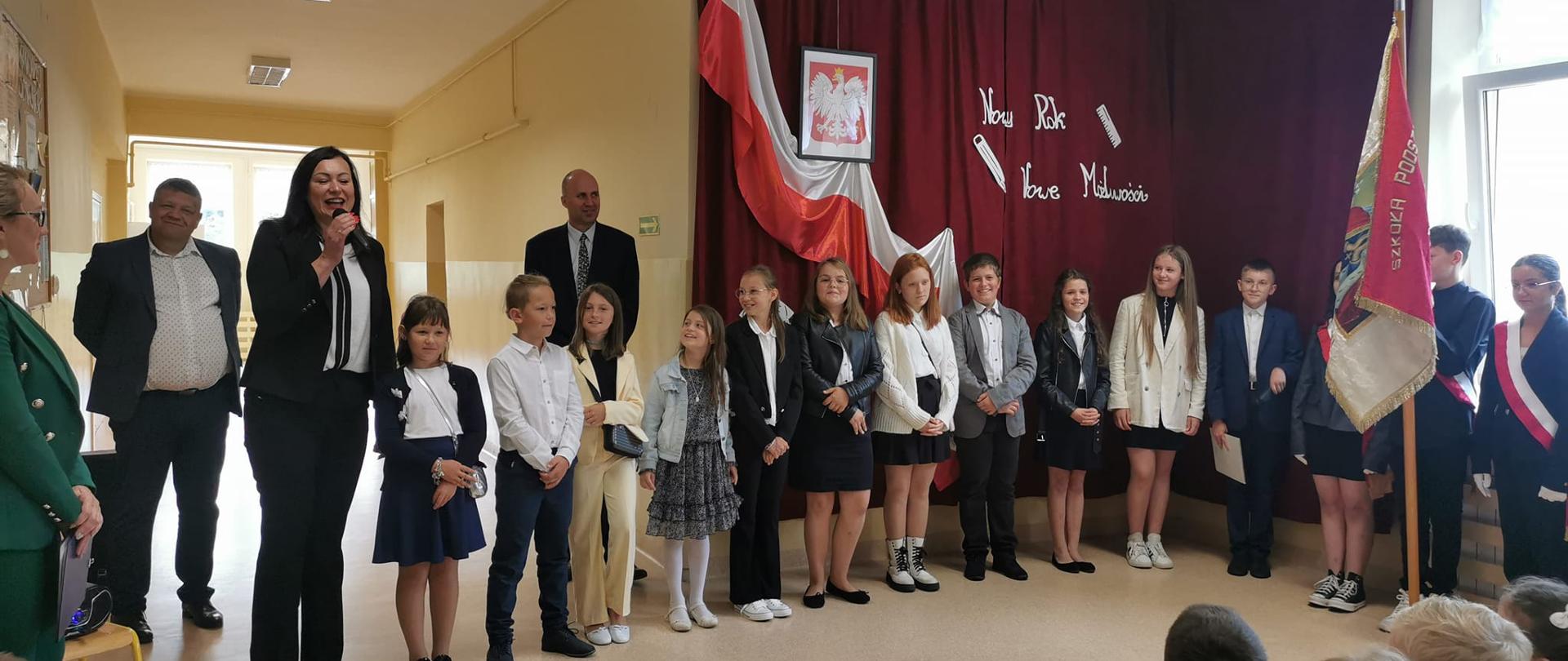 Rozpoczęcie roku szkolnego w Szkole Podstawowej w Maciejowej, Pani Wójt przemawia, po lewej stronie Pani Dyrektor, na środku uczniowie z występem artystycznym, po prawej poczet sztandarowy szkoły
