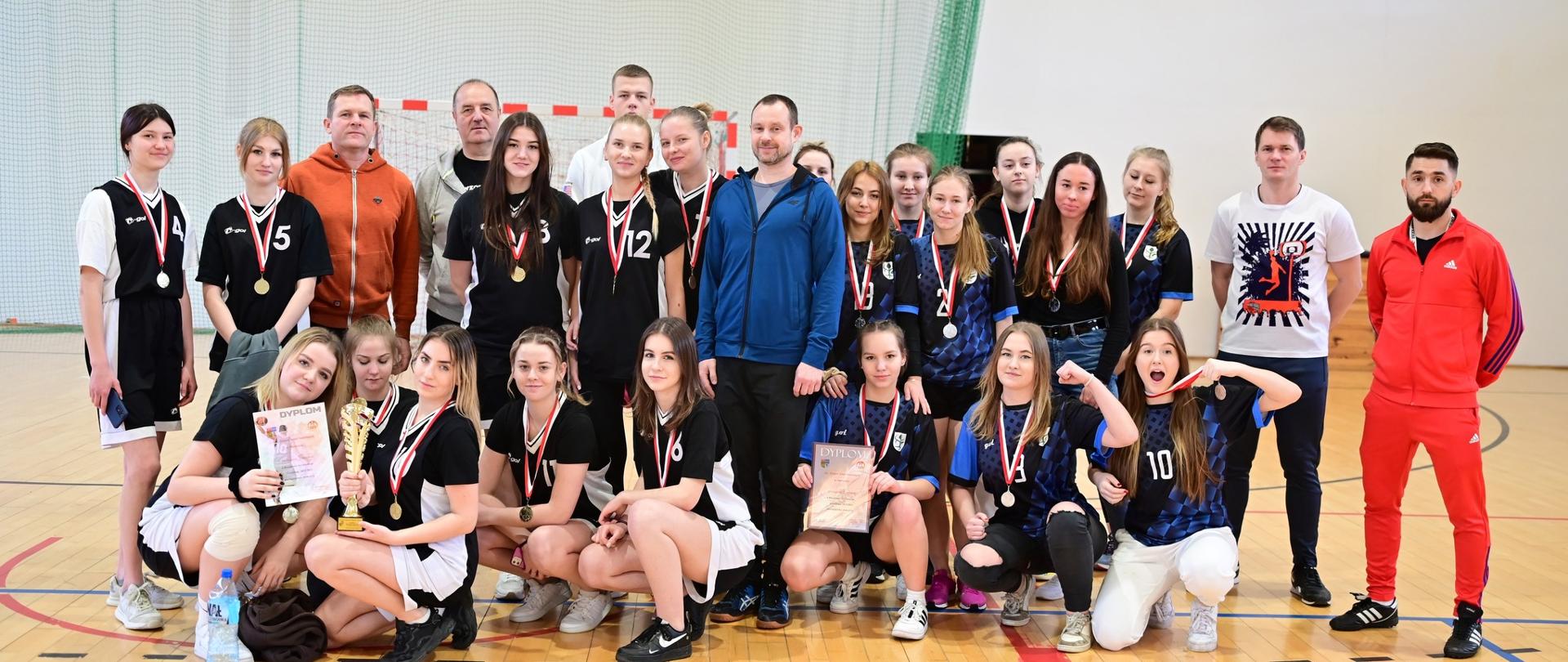 Zdjęcie grupowe zawodniczek z Zespołów Szkół Powiatowych w Chorzelach, trenerów oraz sędziów zawodów.