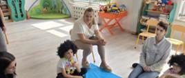 W trakcie zajęć - rodzice z dziećmi siedzą przed niebieską matą, na której leży krokodyl