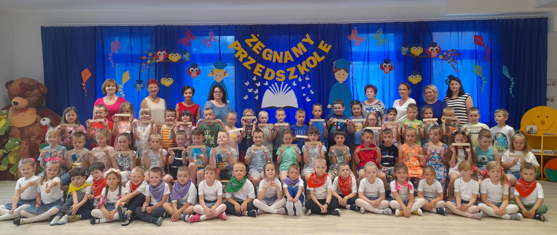 Grupa dzieci z nauczycielami na tle napisu żegnamy przedszkole