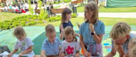na stole leżą różne materiały szkoleniowe przy których stoją dzieci, układają puzzle, rysują długopisami, piękna słoneczna pogoda 