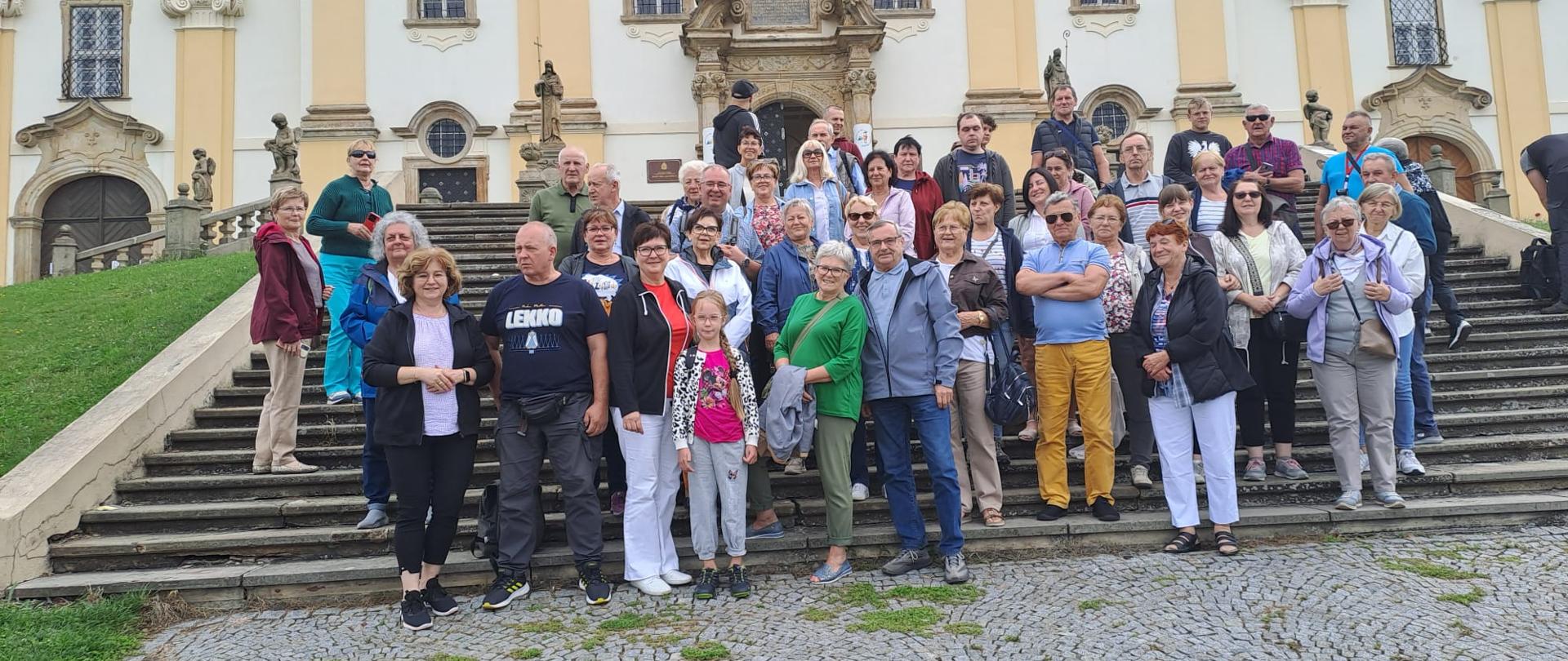 Grupa ludzi pozuje do zdjęcia na schodach przy piaskowym zamku