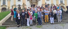 Grupa ludzi pozuje do zdjęcia na schodach przy piaskowym zamku