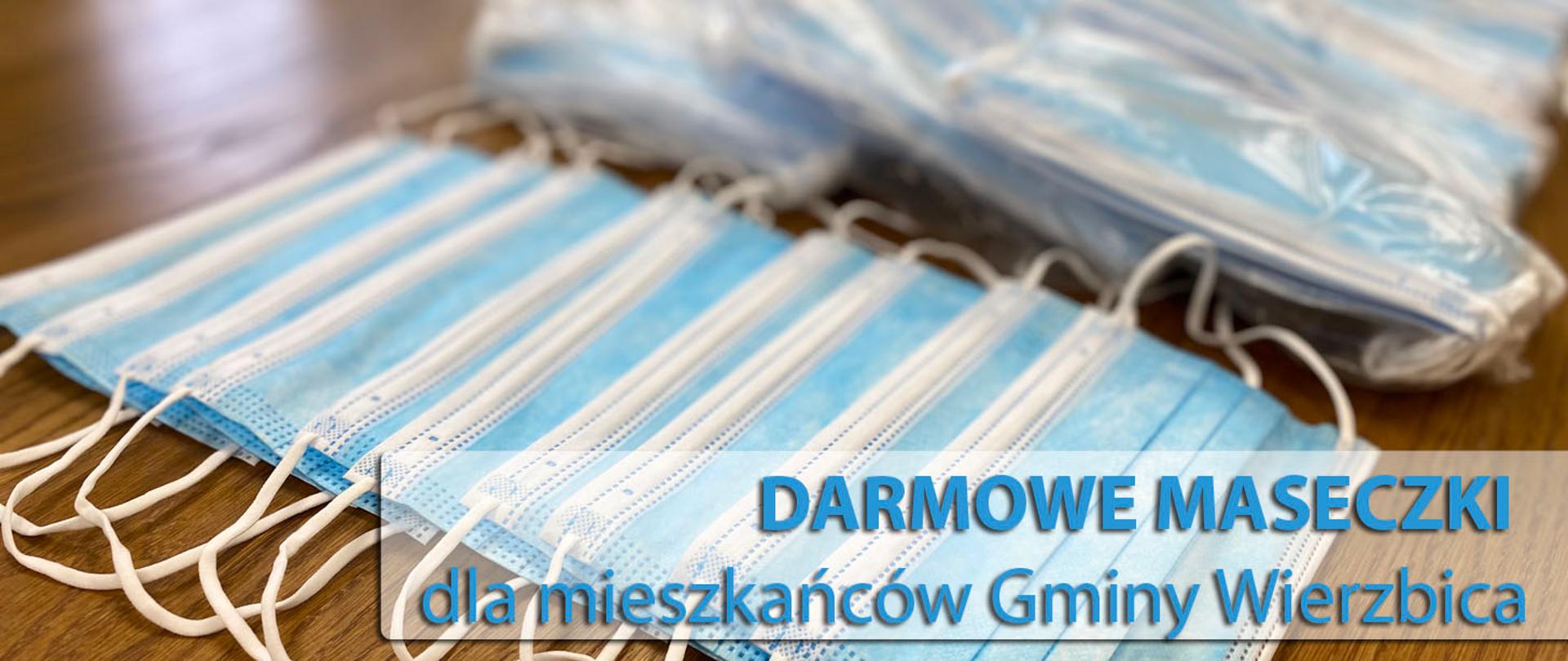 Zdjęcie przedstawia maseczki ułożone na drewnianym stole, oraz napis w kolorze błękitnym o treści "Darmowe maseczki dla mieszkańców Gminy Wierzbica"