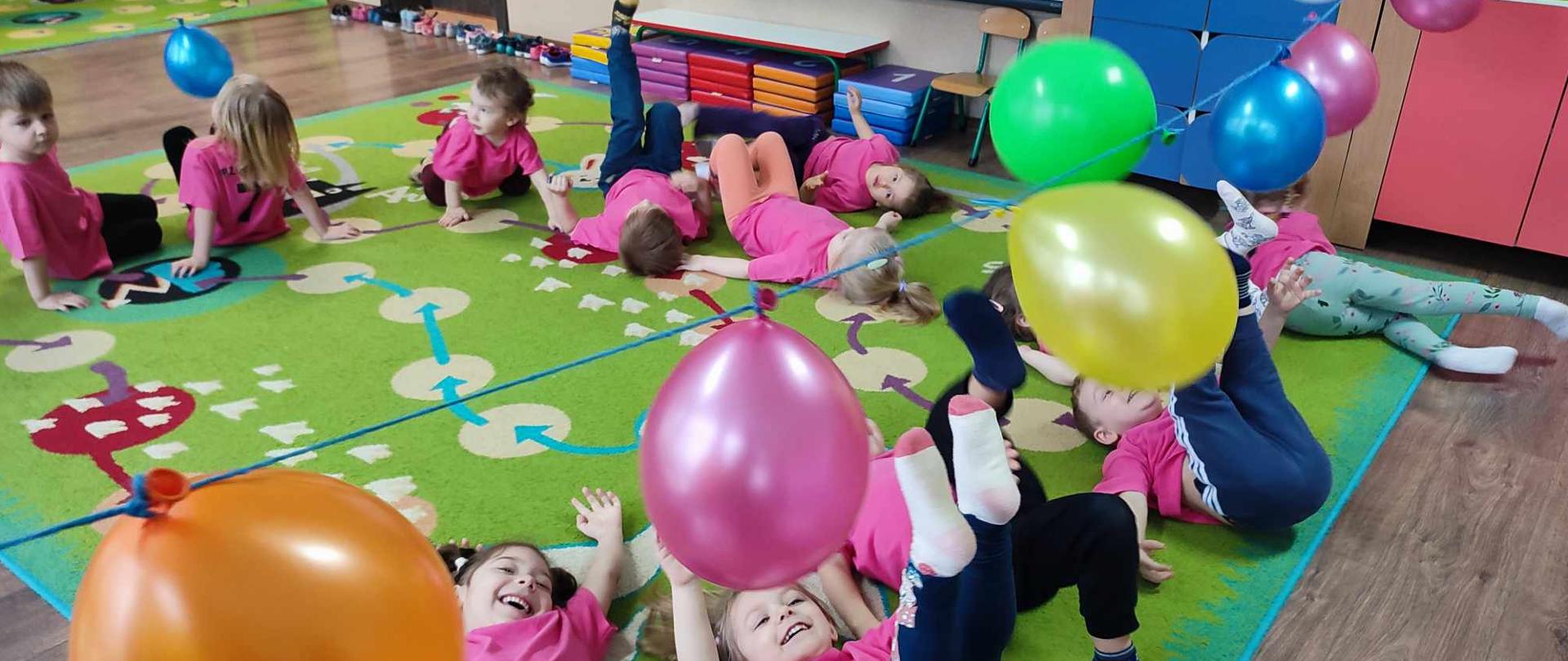 DZIECI WYKONUJĄ ĆWICZENIA GIMNASTYCZNE Z WYKORZYSTANIEM BALONÓW