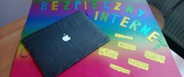 Kolorowy plakat z elementem 3D - otwarty laptop, na kolorowym tle hasłami dotyczącymi bezpieczeństwa w internecie.