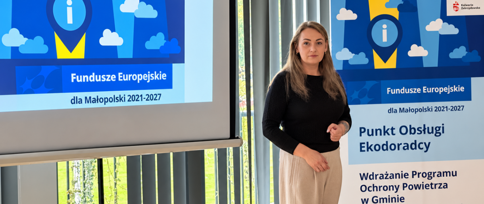 Kobieta w czarnej bluzce i beżowych spodniach stoi przed ekranem projekcyjnym z wyświetloną prezentacją, za nią baner promujący punkt obsługi ekodoradcy