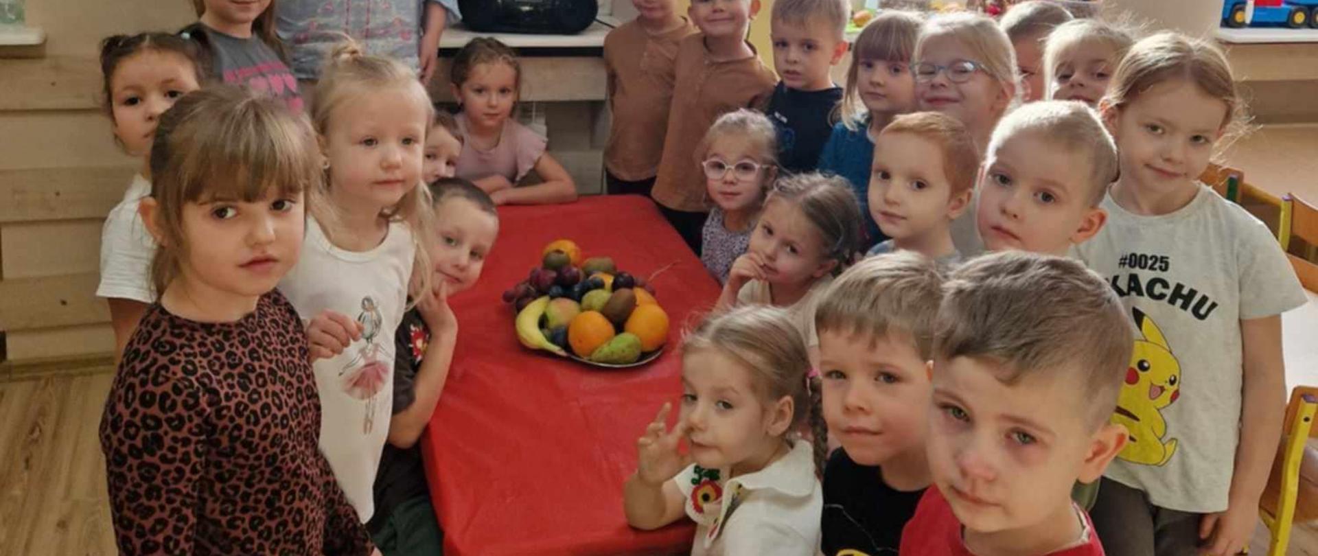 Grupa dzieci i nauczyciel przy stole z owocami