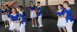 chłopcy i dziewczynki w biało niebieskich strojach tańczą 
