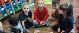 Dzieci z oddziału przedszkolnego siedzą na podłodze wokół makiet pieniążków zakupionych w ramach grantu