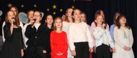 kilkanaście dziewczynek stoi na scenie i śpiewa