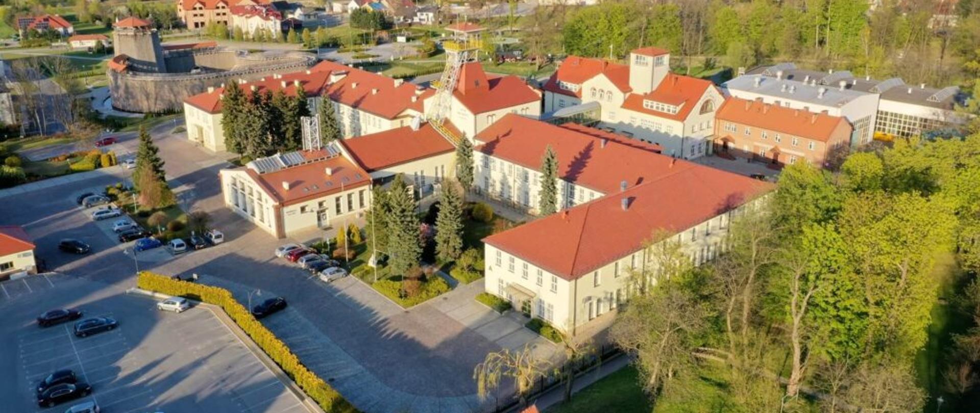 Widok z lotu ptaka na rozległy jasny budynek z czerwonym dachem. 