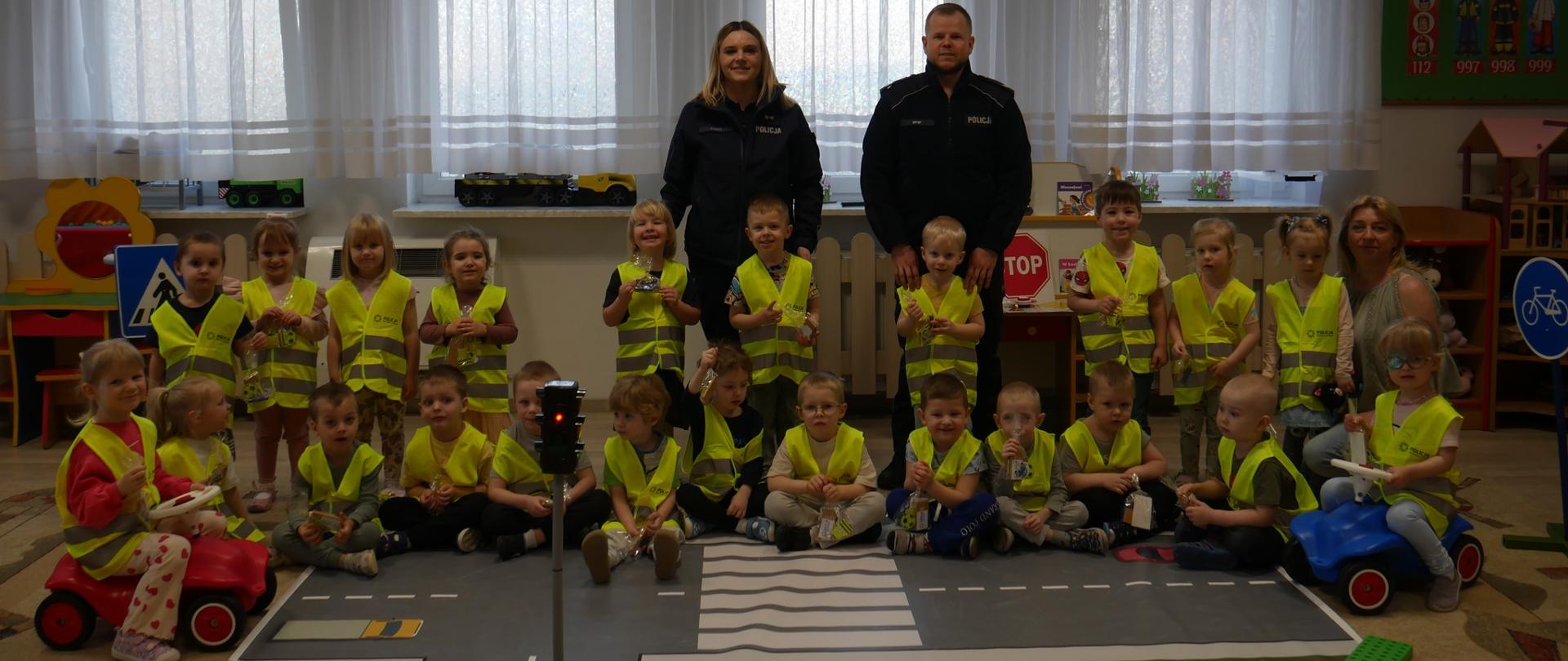 Dwoje policjantów, 1 dorosła i grupa dzieci w koszulkach odblaskowych