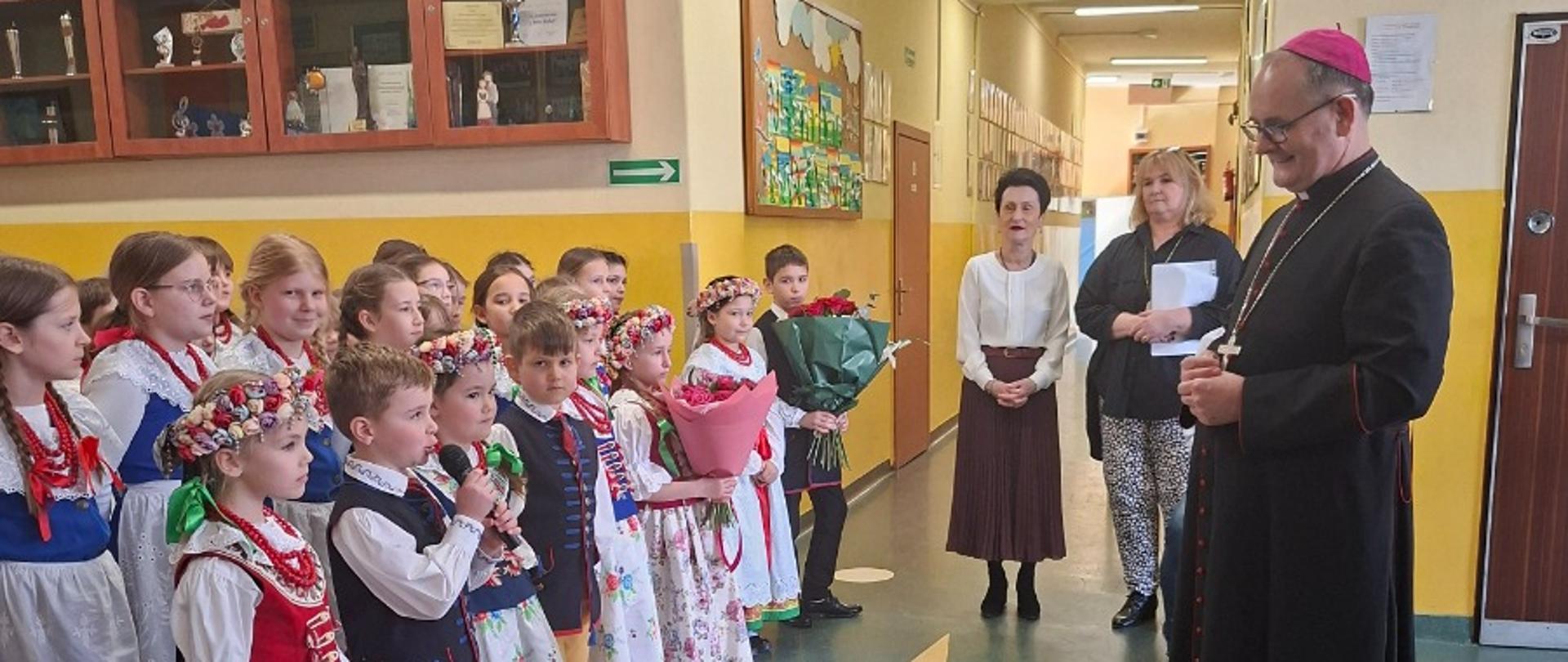 Dzieci stoją przed biskupem na korytarzu szkoły
