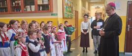Dzieci stoją przed biskupem na korytarzu szkoły