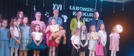 Na scenie stoją zwycięzcy konkursu piosenki, za nimi stoi jury konkursu