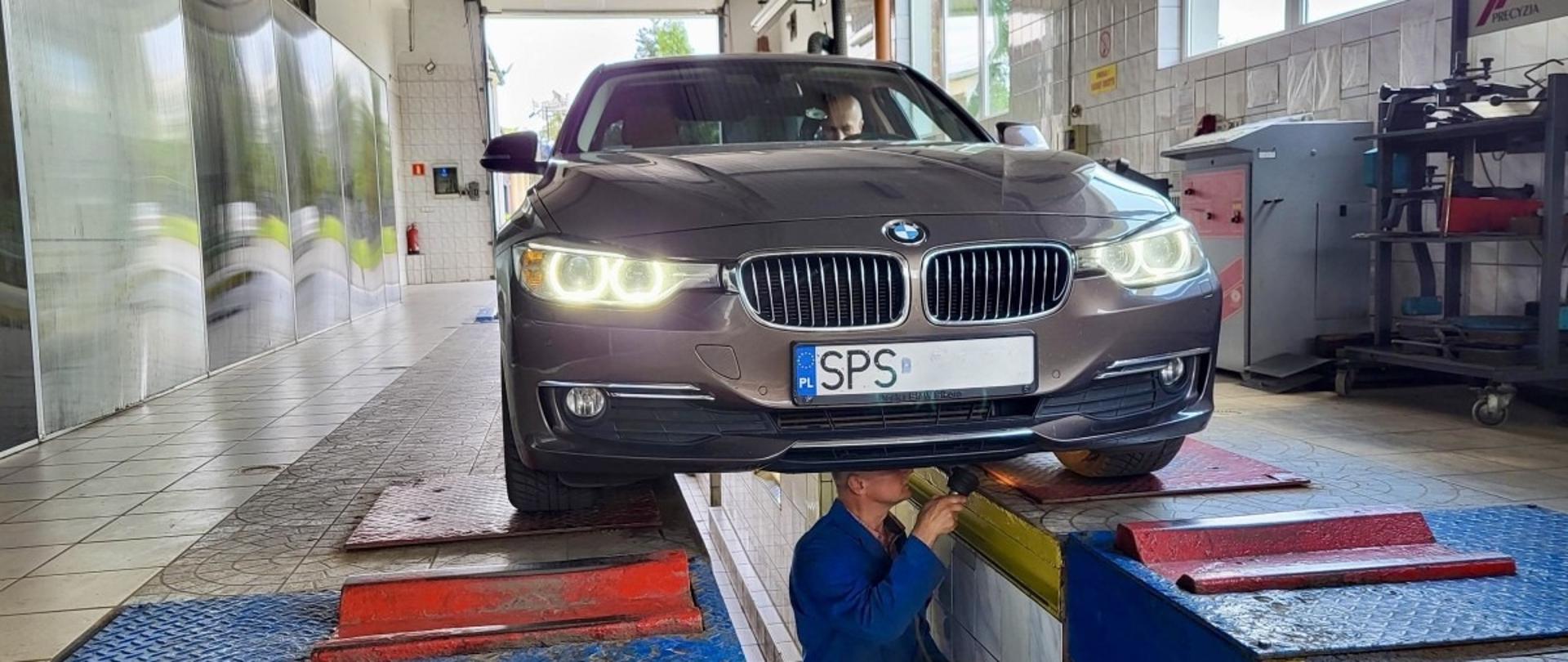 Ciemny samochód stojący w garażu na kanale. W kanale mechanik sprawdza zawieszenie samochodu.