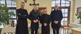Mężczyźni pozują do zdjęcia. W tle żółta ściana na której wisi krzyż