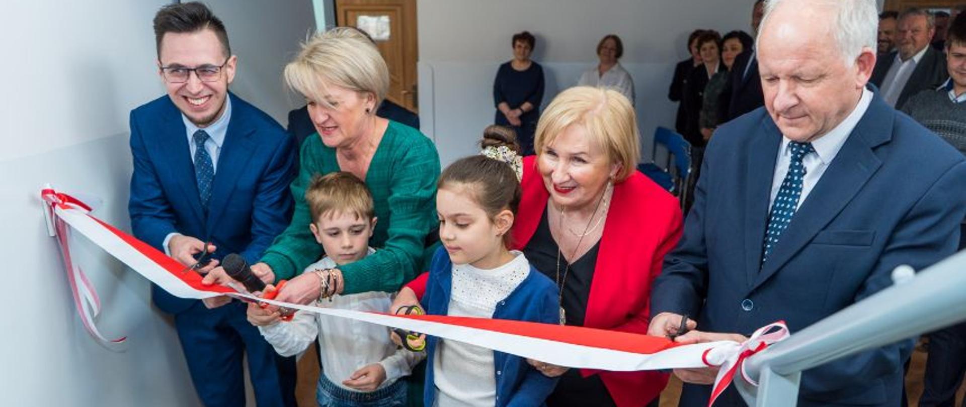 Moment przecięcia wstęgi biało-czerwonej, na zdjęciu Poseł RP Filip Kaczyński, Burmistrz Miasta Augustyn Ormanty, radni Rady Miejskiej, Wicekurator Małopolskiej Oświaty Halina Kumor, Dyrektor Szkoły Beata Zając dwója dzieci.