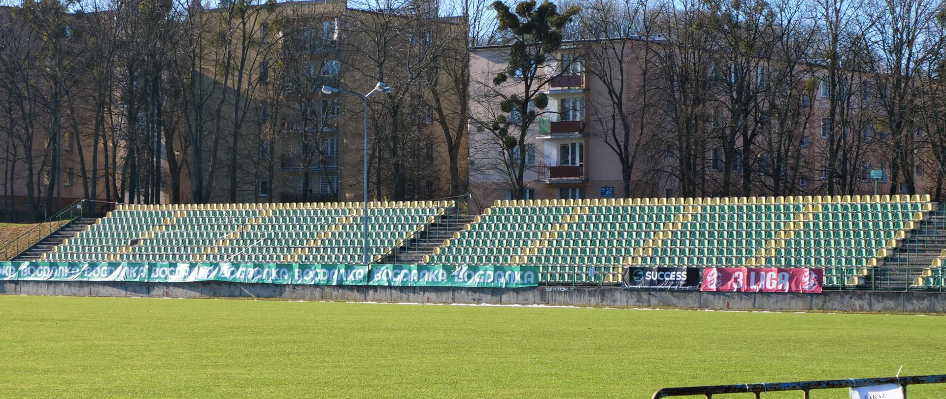 Zdjęcie przedstawia trybuny stadionu piłkarskiego oraz murawę trawiastą na pierwszym planie