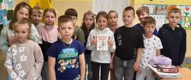 Uczniowie stoją w klasie. Jedna osoba trzyma książkę.