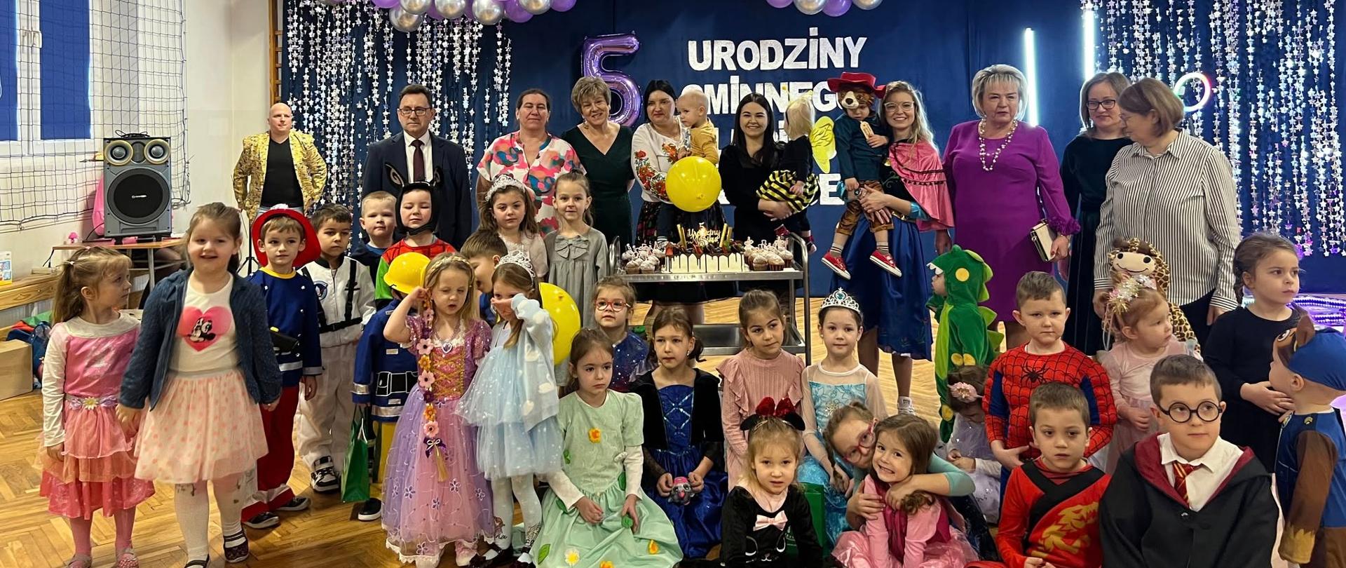 Na zdjęciu widzimy na tle jubileuszowej kolorowej ścianki, zgromadzonych wokół urodzinowego tortu społeczność klubu. Dyrekcję, rodziców, pracowników, dzieci przedstawicieli samorządów. 