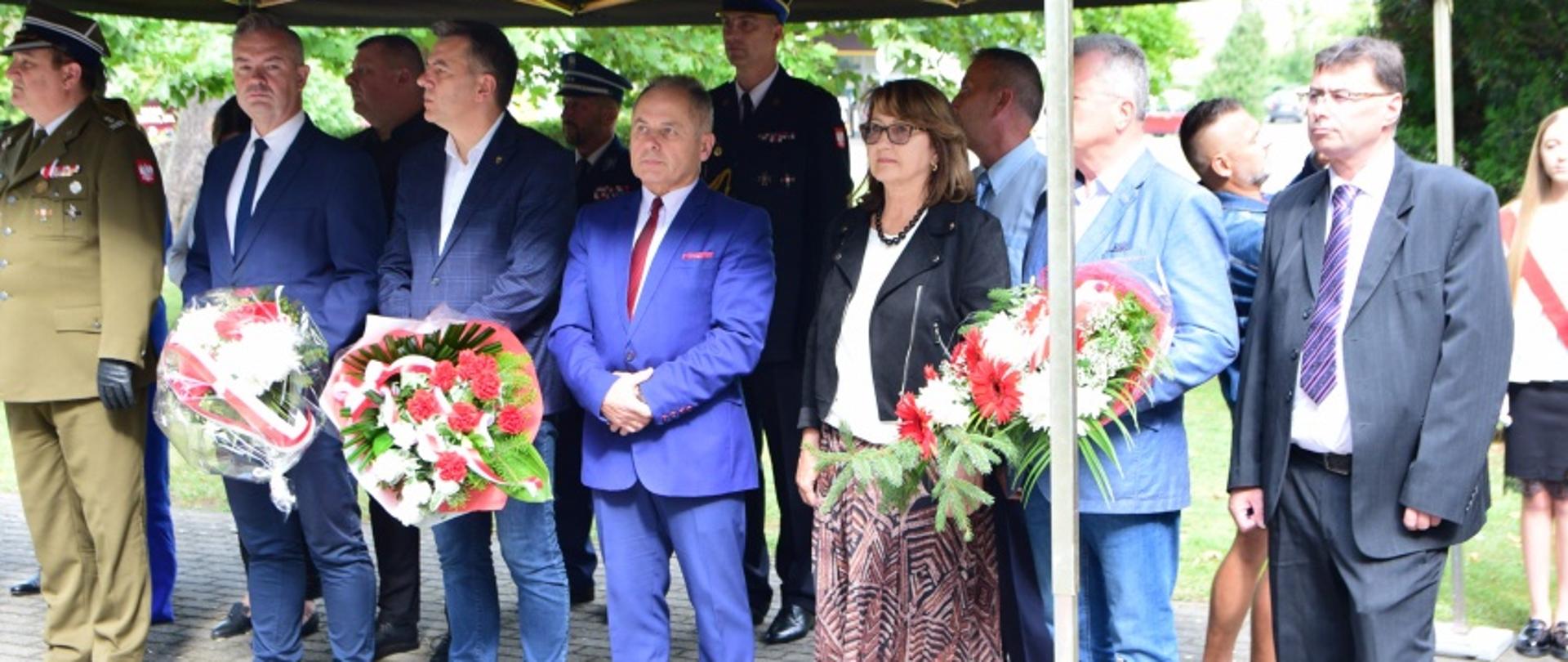 Delegacje stoją pod namiotem, czekając z wieńcami na złożenie ich pod pomnikiem