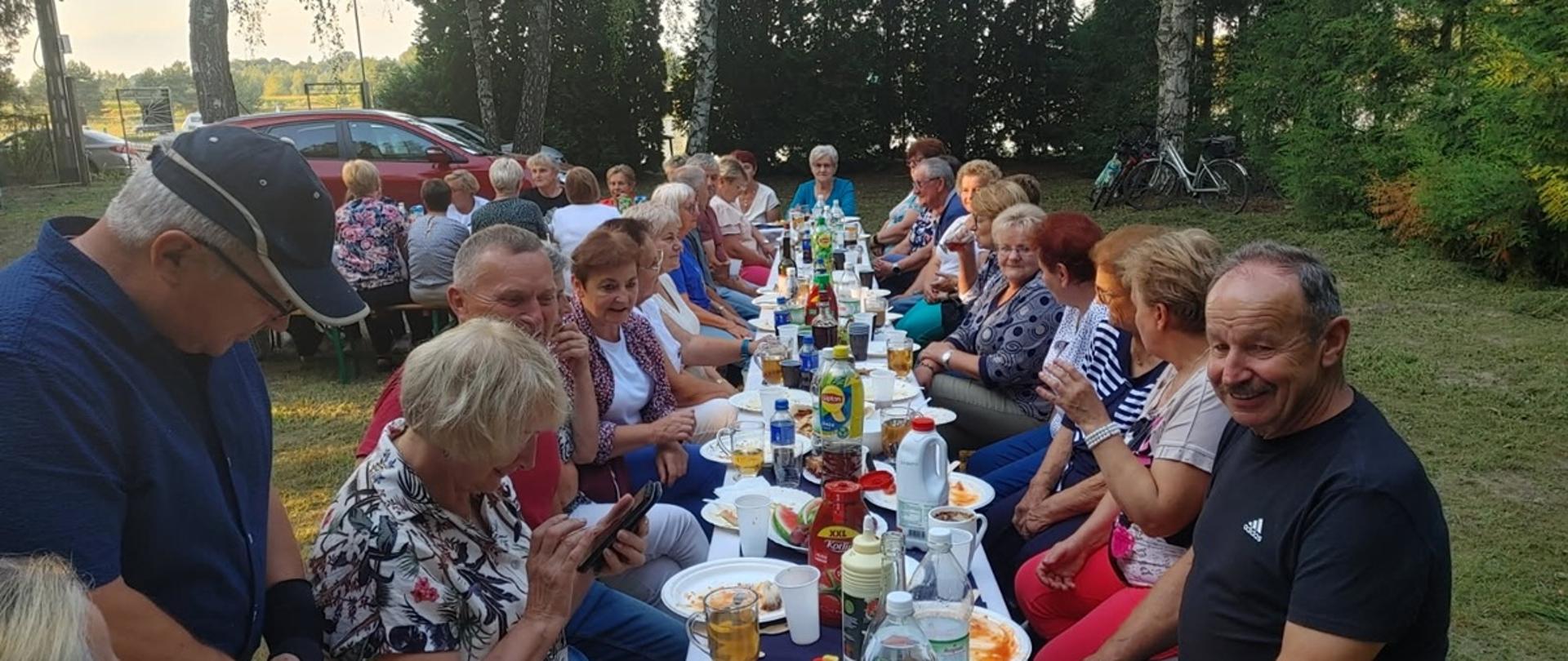 seniorzy kobiety i mężczyźni siedzą przy wspólnym stole zastawionym różnymi przysmakami, i milo spędzają czas 