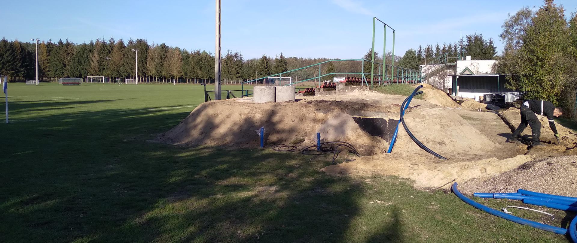 zdjęcie stadionu w Margoninie, widok na częściowo zakopany betonowy zbiornik na deszczówkę, w tle trybuny