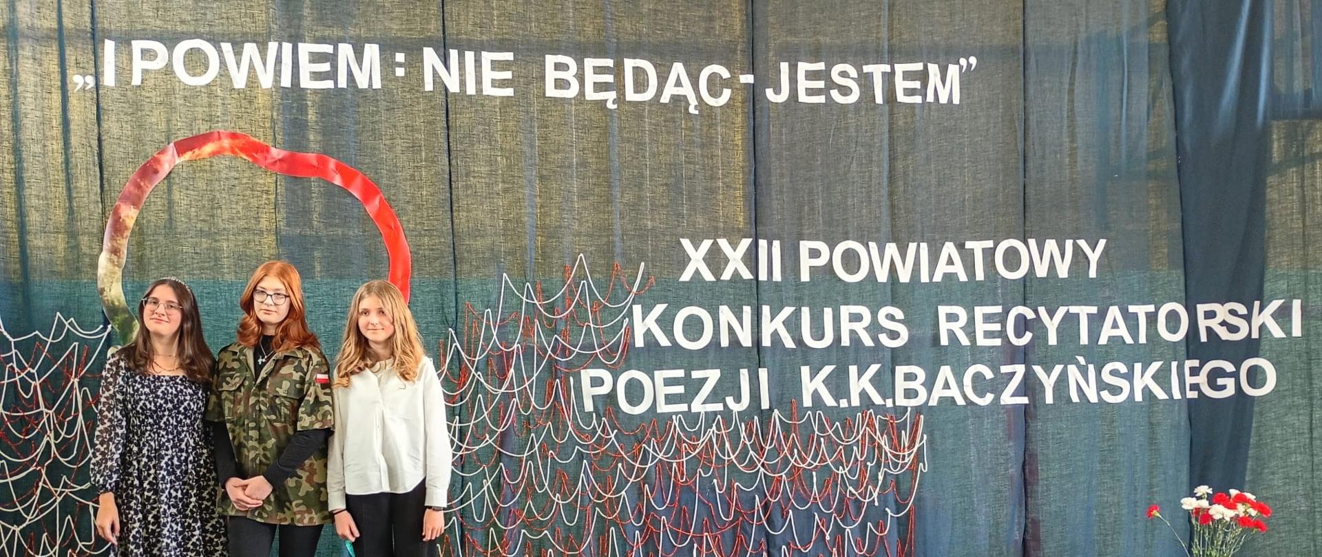 3 stojąca obok siebie dziewczyny. Za nimi biały napis: i powiem nie będąc jestem. XXII Powiatowy Konkurs Recytatorski Poezji K.K. Baczyńskiego