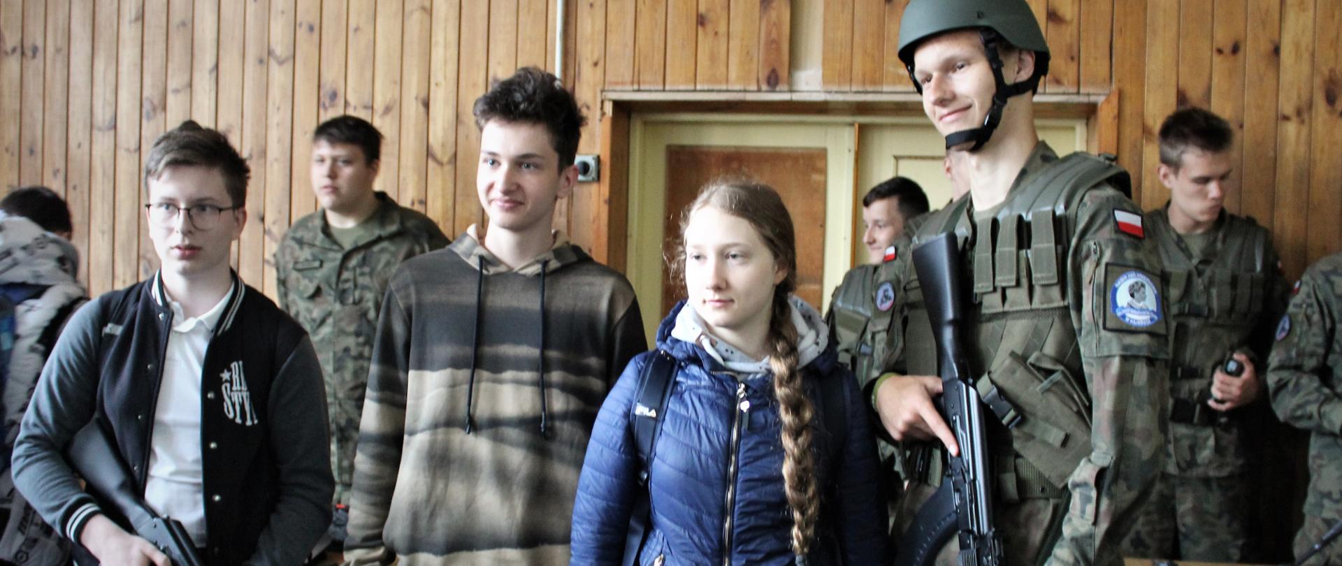 Uczniowie szkół podstawowych pozują do zdjęcia wraz z uczniem Oddziału Przysposobienia Wojskowego 