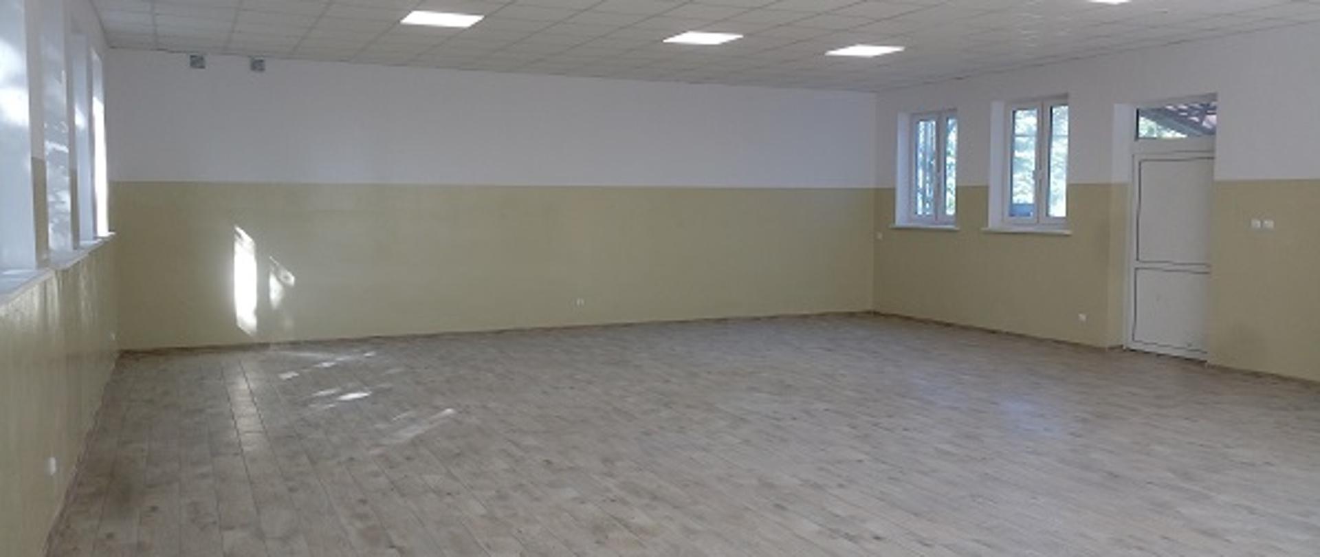 Na zdjęciu widoczne wnętrze sali w remizie OSP Nowe Budy. Ściany pomalowane na kolor biały i ecru. Podłoga i sufit w jasnym kolorze.