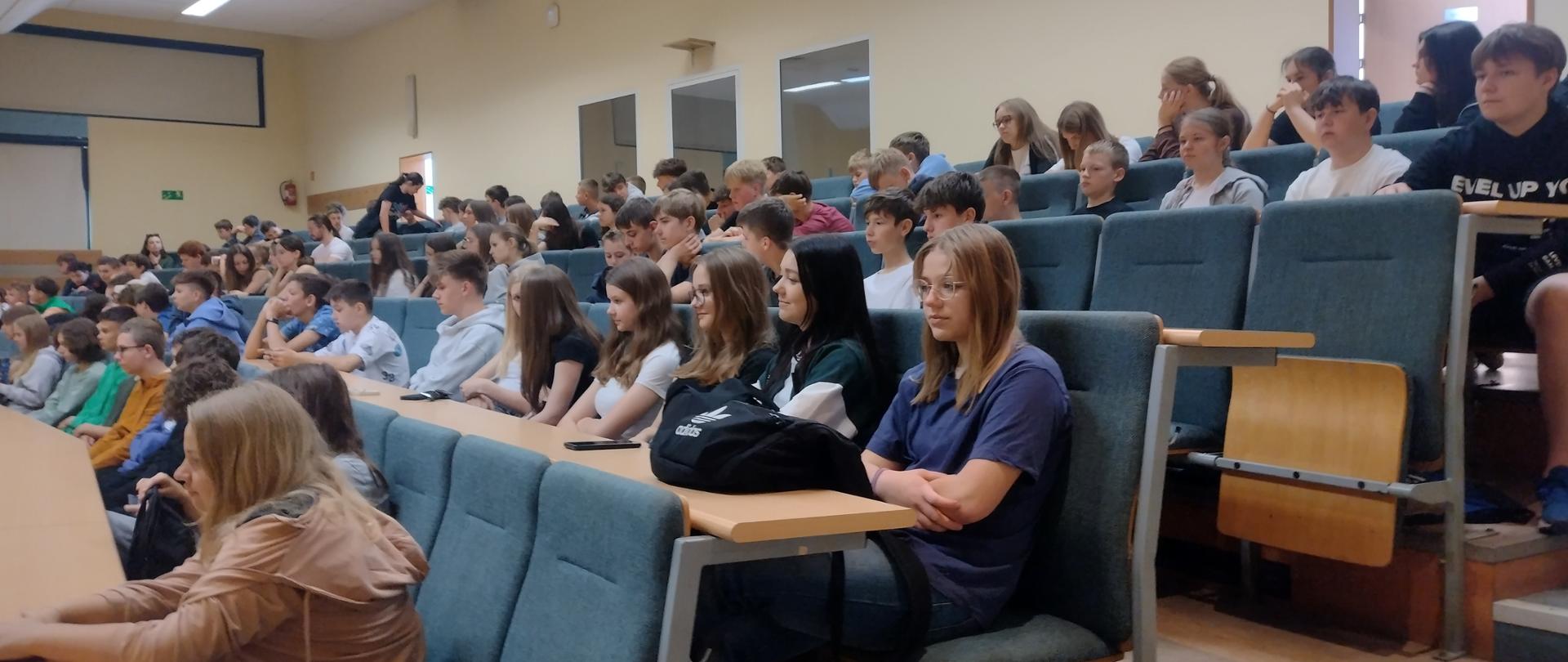 Uczniowie naszej szkoły siedzą na auli i czekają na rozpoczęcie pokazów.