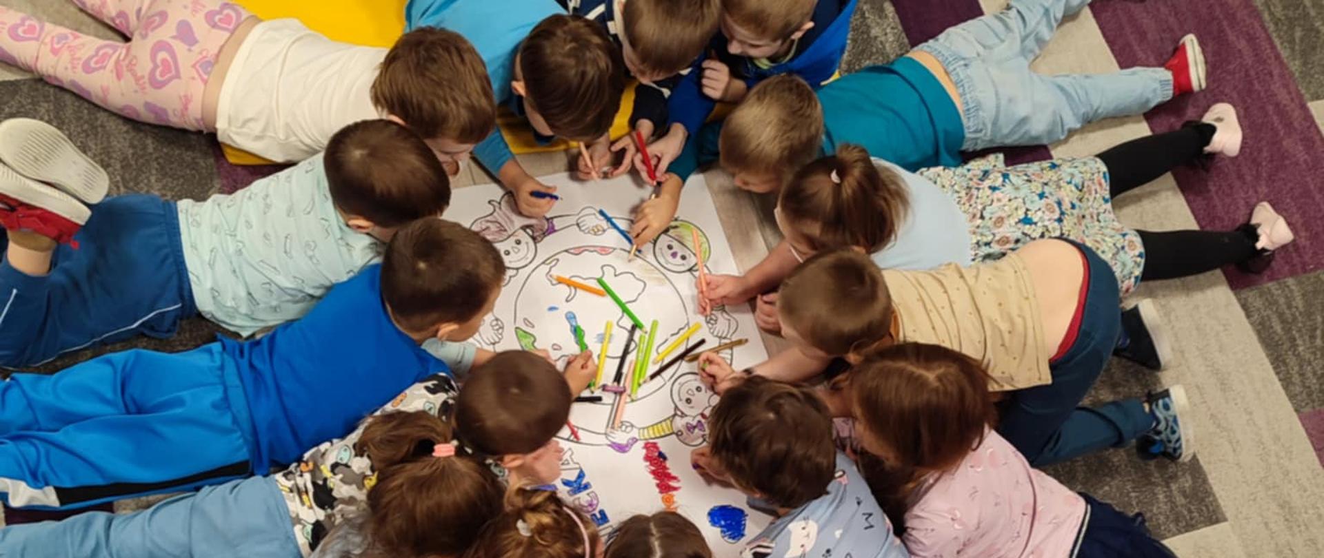 Dzieci w trakcie zabawy - leżą w kółku, wspólnie rysują