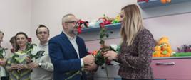 Zdjęcie przedstawia Starostę Krzysztofa Bieńkowskiego wręczającego czerwoną różę pracownicy Powiatowego Centrum Pomocy Rodzinie.