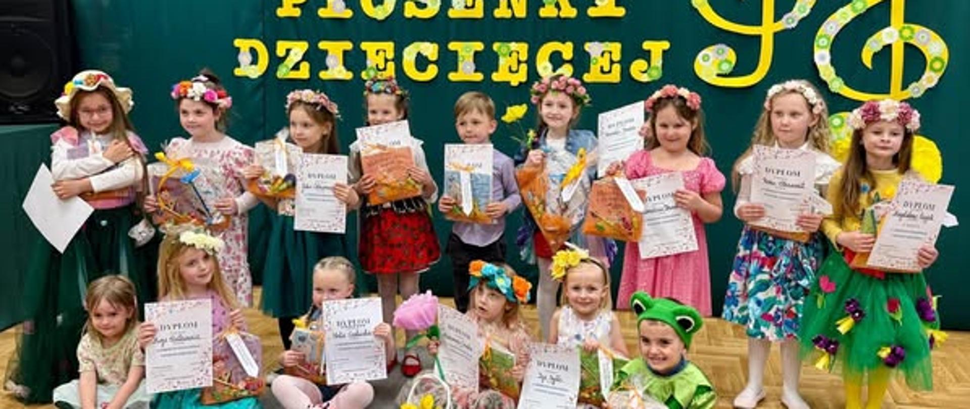 dzieci stoją w dwóch rzędach z dyplomami i nagrodami