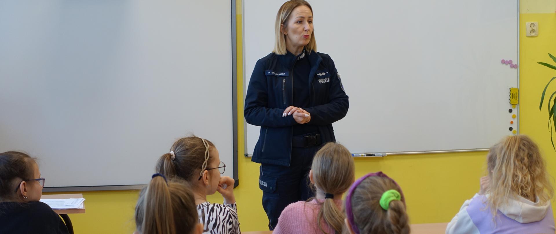 Uczniowie klas I-III w sali lekcyjnej słuchają prelekcji pani policjantki