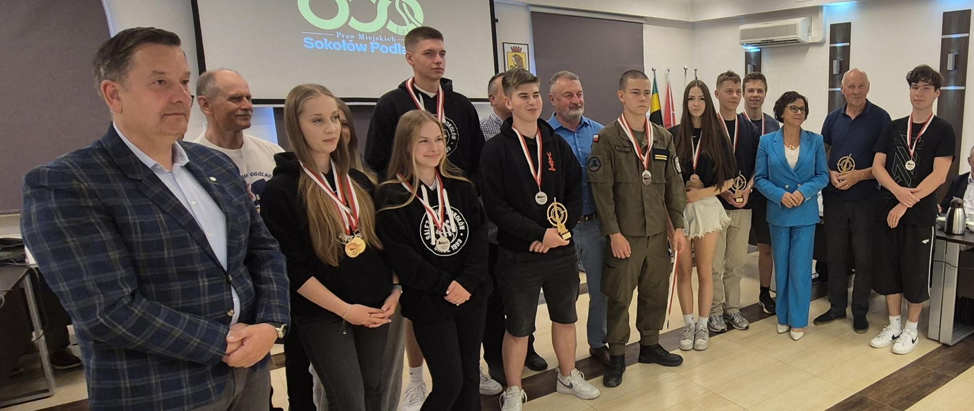 Na zdjęciu widzimy grupę uczniów ze szkół ponadpodstawowych (dziewczęta i chłopcy), którzy zostali uhonorowani statuetkami oraz medalami wraz z przedstawicielami samorządów powiatowego oraz miejskiego, nauczycielami i organizatorami zawodów.