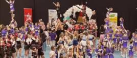 Pokaz kilku drużyn cheerleaderek, które tworzą z siebie różnego rodzaju piramidy, na szczycie każdej stoi jedna dziewczynka