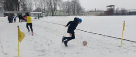 Zabawy na śniegu - dzieci pokonują tor przeszkód kopiąc piłkę