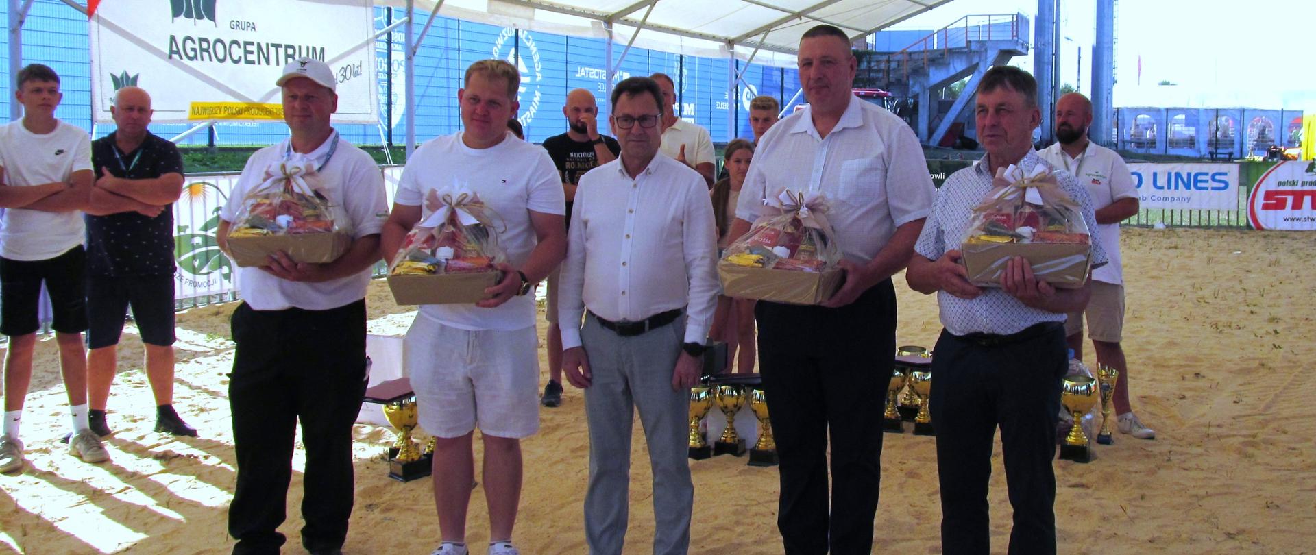 Fotografia wykonana podczas Dni z Doradztwem Rolniczym w Siedlcach.
Na zdjęciu stoją w środku starosta, z każdej strony po dwóch rolników, trzymają w ręku kosze upominkowe, wyróżnienie najlepszy hodowca bydła mlecznego z terenu województwa mazowieckiego.