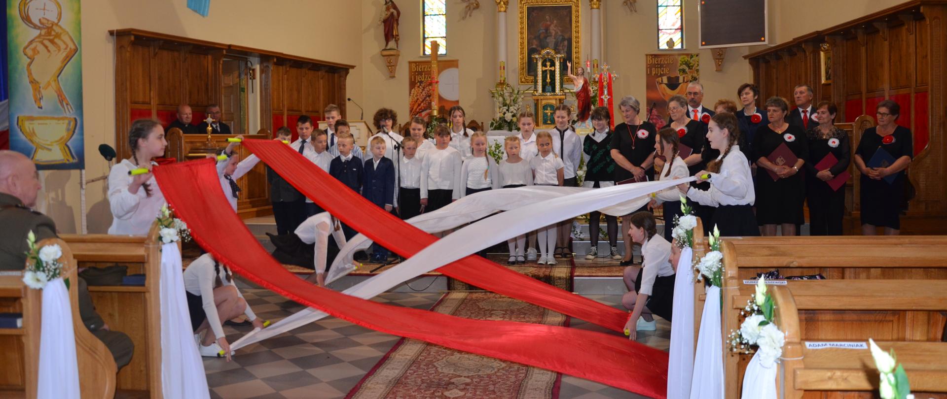 Grupa dzieci w trakcie występu trzymają w rękach szarfy w kolorach flagi państwowej