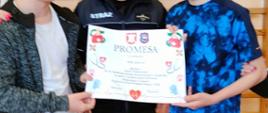 Dwóch uczniów trzyma promesę otrzymaną od pani wójt Gminy Łabowa za zajęcie I miejsca w grze terenowej, za nimi stoi prezes OSP w stroju strażaka