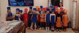 Grupa dzieci w kolorowych fartuchach pozuje do zdjęcia razem z panią nauczycielką.