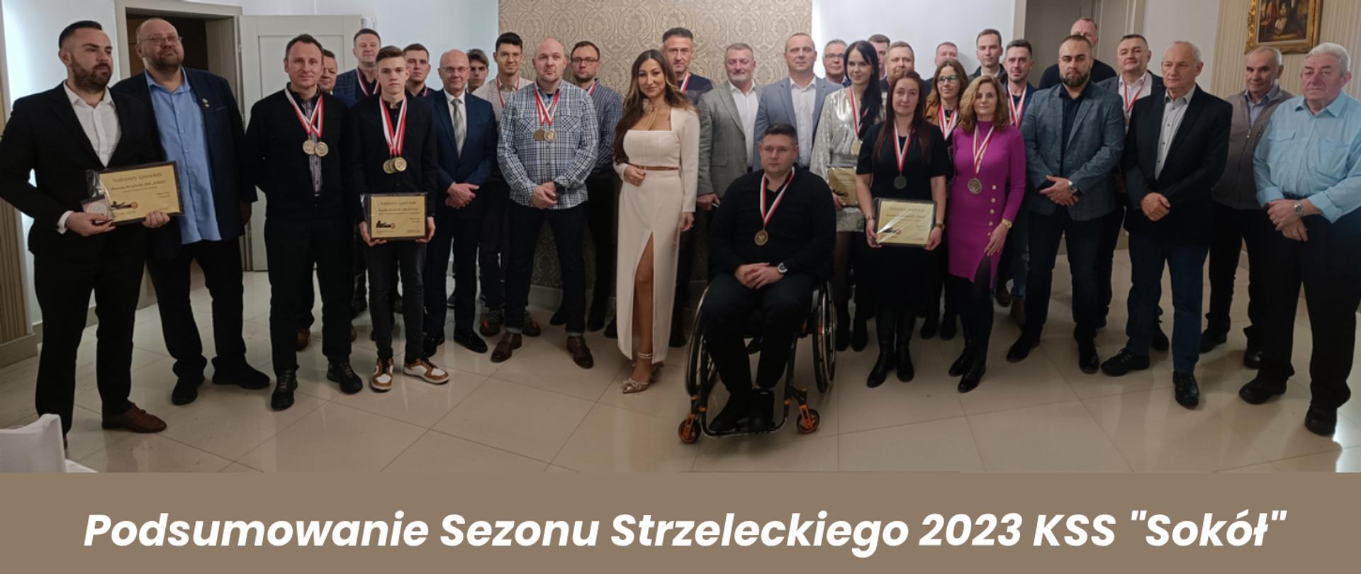 Zdjęcie grupowe wszystkich wyróżnionych zawodników z członkami i zarządem Klubu Strzelectwa Sportowego Sokół oraz zaproszonymi gośćmi, którzy wręczali wyróżnienia. Nagrodzeni zawodnicy na szyjach mają zawieszone medale oraz prezentują zdobyte dyplomy.