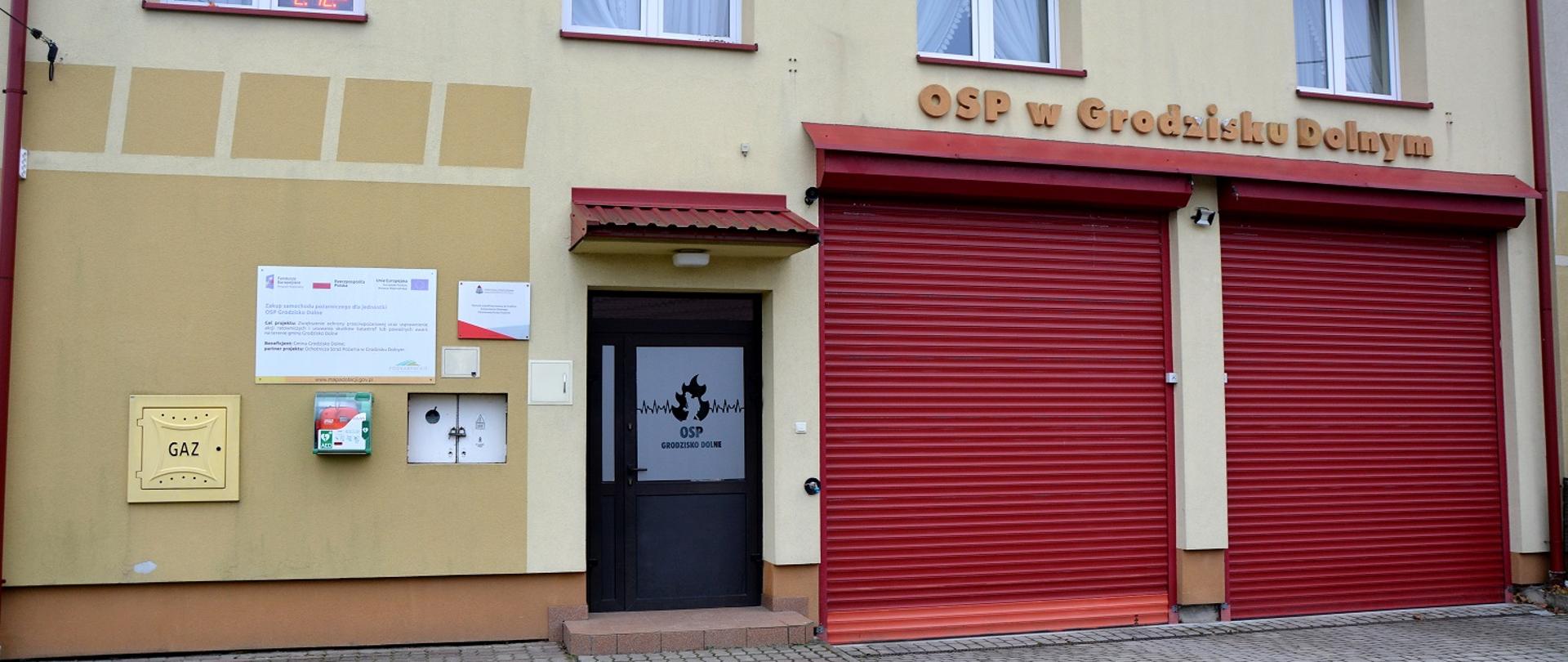 bezowy budynek remizy dwie duże czerwone bramy garażowe na górze białe okna 