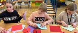 trzy dziewczynki składające z papieru kolorowe serduszka origami