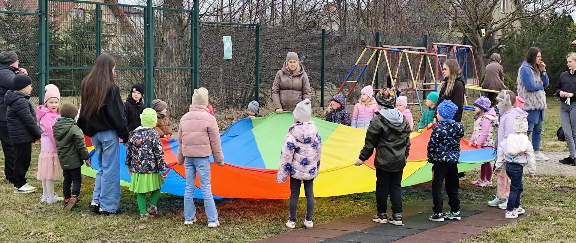 Dzieci z Oddziału Przedszkolnego A i B wraz z Paniami wspólnie bawią się chustą animacyjną.
