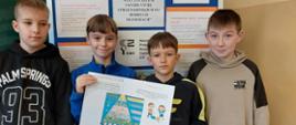 Czterech uczniów trzyma wspólnie własnoręcznie wykonany plakat mówiący o zasadach kulturalnego zachowania, za nimi ścianka moderacyjna z zasadami savoir-vivre